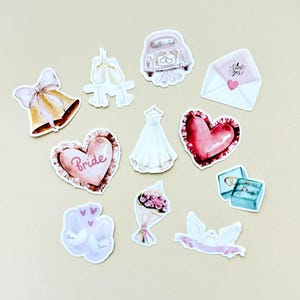 Könnte beinhalten: Eine Sammlung von Aufklebern im Aquarellstil mit Hochzeitsmotiven. Enthält eine Glocke, Ballettschuhe, ein Oldtimer-Auto, einen Umschlag mit "Said yes!", ein Herz, ein Brautkleid, einen Blumenstrauß und eine Taube.