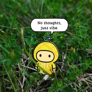 May include: A yellow enamel pin depicting a cartoon pineapple in a hoodie, with the text "No thoughts, just vibe" in a speech bubble. The pin is set against a background of green grass and foliage.