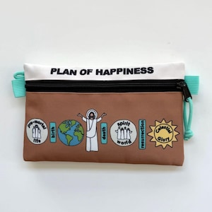 May include: A brown and white zippered pouch with the text "PLAN OF HAPPINESS". The pouch features illustrations of a person, the Earth, and other religious symbols. It has a black zipper and teal pull tabs.