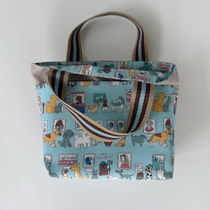 May include: A light blue tote bag with a repeating pattern of various dog illustrations. The bag has brown and blue striped handles and a gray trim. The text "Please Keep Going" is visible on the front of the bag.