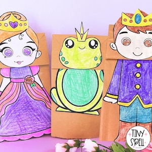 May include: Three brown paper bag puppets featuring hand-colored illustrations of a princess with a gold crown, a green frog with a gold crown, and a prince with a gold crown. The prince puppet has a purple jacket and blue pants. A logo reads Tiny Spell Studio.