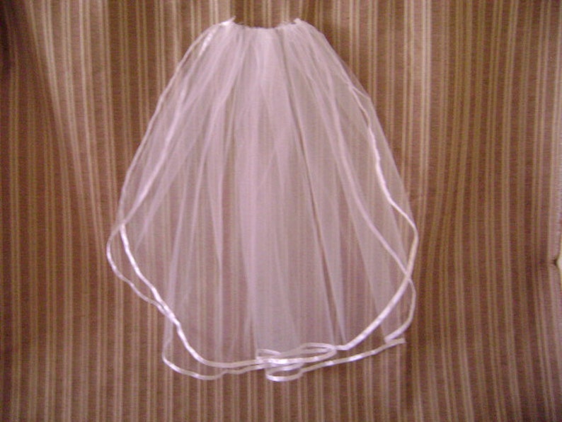 Pu&ograve; includere: Un velo da sposa bianco in tulle sottile. I bordi del velo sono rifiniti con un nastro di raso. Questo velo &egrave; progettato per matrimoni o eventi speciali, offrendo un aspetto classico ed elegante. Un accessorio nuziale tradizionale.