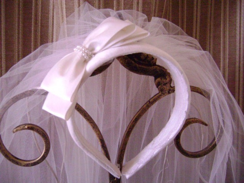 Pu&ograve; includere: Una fascia per capelli da sposa bianca con un grande fiocco di raso e un velo delicato. Il fiocco &egrave; adornato con piccole perle. Il velo &egrave; realizzato in un tessuto trasparente e leggero.