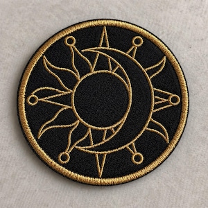 May include: Embroidered patch featuring a celestial design. The patch has a black background with a gold sun and crescent moon design. The sun and moon are surrounded by gold accents. The patch is circular with a gold border.