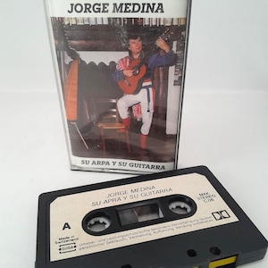 May include: A vintage cassette tape and case featuring the album "Su Arpa y Su Guitarra" by Jorge Medina. The cassette is black with yellow accents and white labels. The case shows a man playing a guitar.