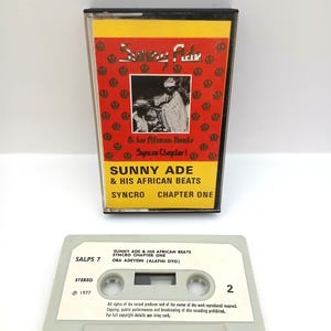 May include: Two vintage cassette tapes. One is in a clear case with a red and yellow label featuring the text "Sunny Ade & His African Beats." The other tape is light grey with black text, including the album title and artist.