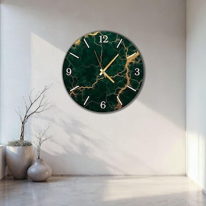 Könnte beinhalten: Eine runde Wanduhr mit dunkelgrünem Marmormuster und goldenen Akzenten. Das Zifferblatt hat weiße Ziffern und goldene Zeiger. Die Uhr ist an einer weißen Wand befestigt.