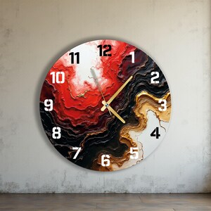 Puede incluir: Reloj de pared redondo con un diseño abstracto vibrante. La esfera del reloj presenta una mezcla de colores rojo, negro, dorado y blanco, con grandes números blancos. Las manecillas del reloj son doradas.