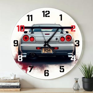 Op de afbeelding: Een ronde wandklok met een zilveren sportwagen met rode achterlichten en een achterspoiler. De klok heeft zwarte cijfers en wijzers, met de nummerplaat van de auto met "R34". De achtergrond heeft een aquareleffect.