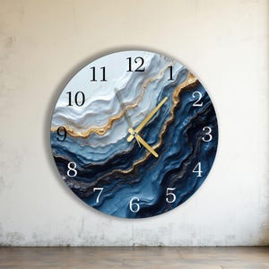 Puede incluir: Reloj de pared redondo con un diseño abstracto azul, blanco y dorado. La esfera del reloj presenta números negros y manecillas doradas. El diseño se asemeja a piedra o mármol en capas.