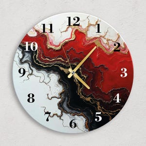 May include: Circular wall clock with an abstract design in white, red, black, and gold. The clock face has black numerals and gold hands. The design resembles a marbled or geode pattern.