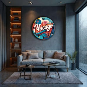 Könnte beinhalten: Eine runde Wanduhr mit einem farbenfrohen Chicago-Design. Das Zifferblatt zeigt das Wort "Chicago" in einer stilisierten Schriftart mit einem Blau-, Rot- und Orangeton. Die Uhr hängt an einer grauen Wand über einem grauen Sofa.