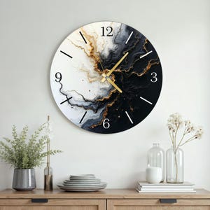 Könnte beinhalten: Runde Wanduhr mit Marmordesign in Schwarz, Weiß und Gold. Das Zifferblatt hat schwarze Ziffern und Zeiger, mit einem goldenen Sekundenzeiger. Die Uhr ist an einer weißen Wand über einem Holzschrank befestigt.