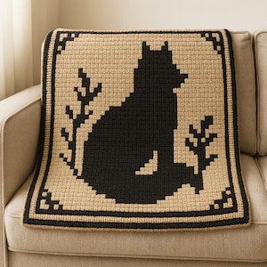 Puede incluir: Una manta tejida a ganchillo en negro y beige con la silueta de un zorro y follaje. La manta tiene un borde negro y se muestra sobre un sofá beige. La manta mide aproximadamente 102 cm cuadrados.