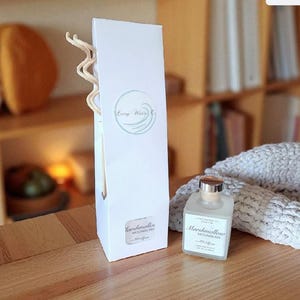 May include: A white box and a small glass bottle of Marshmallow Moonbeam fragrance. The box has a circular logo and the words "Living Waters Co." The bottle has a silver cap and a label that reads "Marshmallow Moonbeam". Reed diffuser sticks are visible.