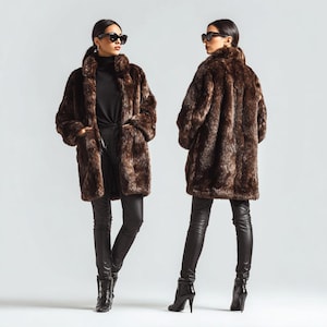 May include: A brown faux fur coat with a textured pattern. The coat has a wide collar and pockets. The model is wearing black pants and boots. The coat is knee-length and appears to be made of a soft material.