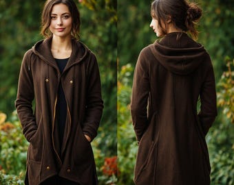 May include: A brown hooded coat with a button closure and pockets. The coat is made of a soft material and has a long, flowing design. The model is wearing a black shirt underneath.