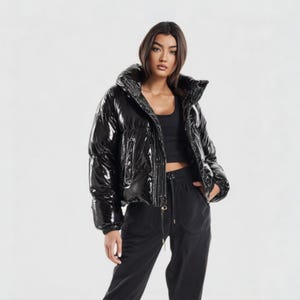 May include: A glossy black puffer jacket with a high collar. The jacket has a shiny, reflective surface and a cropped length. The model is wearing black pants and a black top. The background is plain white.
