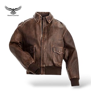 Op de afbeelding: Bruine leren jas met een distressed afwerking, ritssluiting en twee voorzakken. De jas heeft een geribbelde zoom en manchetten, en een klassieke omgeslagen kraag. Het Hawk n Leather-logo is zichtbaar linksboven.