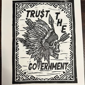 May include: Black and white print featuring a skull wearing a feathered headdress, pierced by an arrow. The text reads "TRUST THE GOVERNMENT" in bold letters, framed by a decorative border. The artwork is on a white background.
