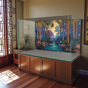Può includere: Un grande acquario in vetro trasparente con uno sfondo a vetrata raffigurante una scena di foresta. L'acquario è posto su un mobile in legno con quattro ante. La scena della foresta presenta alberi, un fiume e un fogliame colorato.