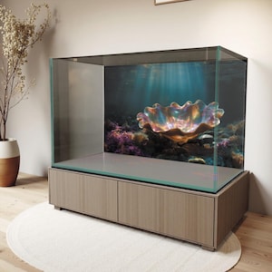 Puede incluir: Un gran acuario rectangular con tapa y laterales de cristal, colocado sobre un mueble de madera clara. El fondo del acuario presenta una escena submarina con una gran concha iridiscente y coral. El mueble tiene dos puertas.