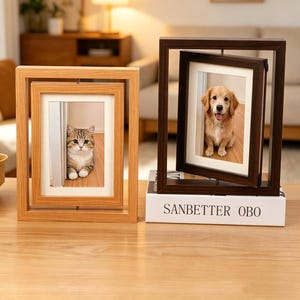 May include: Two wooden photo frames, one light brown and one dark brown, each holding a photograph. The light brown frame has a cat photo, and the dark brown frame has a dog photo. The text "SANBETTER OBO" is visible on a book.