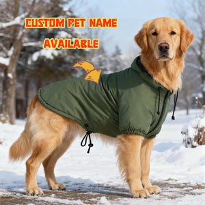 Könnte beinhalten: Ein Golden Retriever trägt einen olivgrünen Hundemantel mit Kapuze, schwarzem Reißverschluss und Kordelzug. Der Text "CUSTOM PET NAME AVAILABLE" wird in orangefarbenen Buchstaben angezeigt. Der Hund steht in einer verschneiten Umgebung.