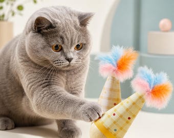 May include: A gray British Shorthair cat plays with two yellow and white cone-shaped cat toys with colorful feather accents. The toys have a wooden base and are decorated with a polka dot and striped pattern.
