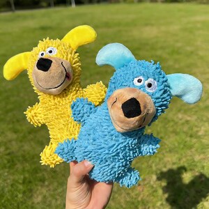 Könnte beinhalten: Zwei Plüschhundespielzeuge. Eines ist gelb mit gelben Ohren, das andere ist blau mit blauen Ohren. Beide haben braune Nasen und lächelnde Gesichter. Die Spielzeuge bestehen aus einem weichen, strukturierten Material und sind für Haustiere konzipiert.