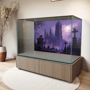 May include: A large glass terrarium with a wooden base. The backdrop features a spooky graveyard scene with a gothic cathedral under a full moon. The terrarium sits on a light-colored wooden cabinet with two doors, and a white rug is beneath it.