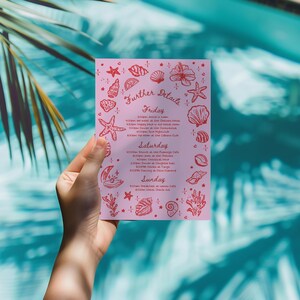 May include: A pink invitation with the words "Further Details" and event information, decorated with red seashell and starfish illustrations. The invitation is held in front of a turquoise pool.