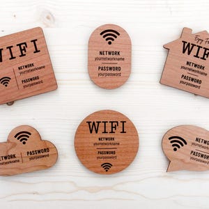 Könnte beinhalten: Verschieden geformte Holzschilder mit WLAN-Passwörtern: quadratisch, oval, Haus, Wolke, Kreis und Sprechblase. Jedes Schild zeigt "WIFI", den Netzwerknamen und das Passwort. Die Schilder sind aus hellbraunem Holz.