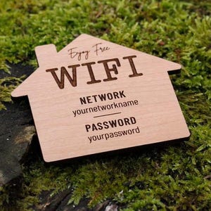 May include: A wooden house-shaped sign with the words "Enjoy Free WIFI" engraved on it. The sign also includes fields for network name and password. The sign is resting on a bed of green moss.