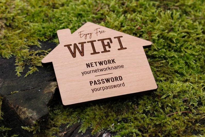 May include: A wooden house-shaped sign with the words "Enjoy Free WIFI" engraved on it. The sign also includes fields for network name and password. The sign is resting on a bed of green moss.