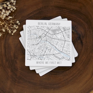 Può includere: Una pila di sottobicchieri quadrati bianchi con una mappa di Berlino, Germania, stampata sul sottobicchiere superiore. Il testo "BERLIN, GERMANY" e "WHERE WE FIRST MET" sono stampati. I sottobicchieri sono su una superficie di legno scuro.