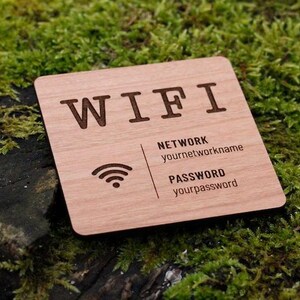 May include: A square wooden sign with the word "WIFI" engraved at the top. Below, it displays "NETWORK" and "PASSWORD" with fields for network name and password. A Wi-Fi symbol is also present. The sign is set against a backdrop of green moss.