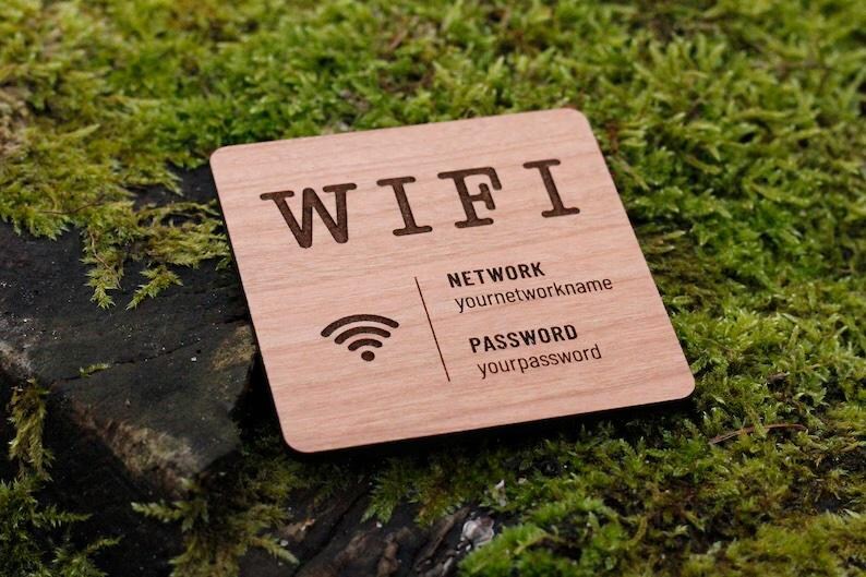 May include: A square wooden sign with the word "WIFI" engraved at the top. Below, it displays "NETWORK" and "PASSWORD" with fields for network name and password. A Wi-Fi symbol is also present. The sign is set against a backdrop of green moss.