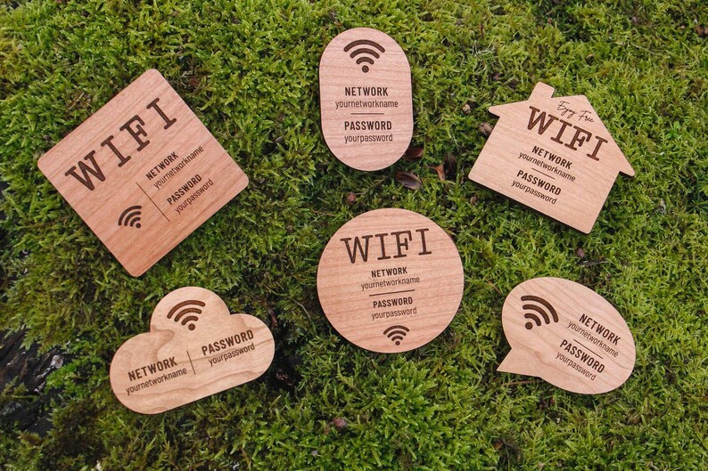 May include: Wooden WiFi password signs in various shapes, including a square, oval, house, cloud, circle, and speech bubble. Each sign has the word "WIFI", network name, and password printed on it. The signs are on a bed of green moss.