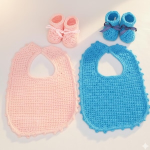 Könnte beinhalten: Eine Sammlung handgefertigter Babyartikel, darunter zwei Paar gehäkelte Babyschuhe mit Schleifen und zwei gehäkelte Lätzchen. Ein Lätzchen und ein Paar Schuhe sind hellrosa, das andere Lätzchen und die Schuhe sind hellblau.