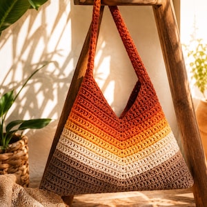 May include: A triangular crochet shoulder bag featuring a chevron pattern with horizontal stripes in gradient shades of dark brown, beige, yellow, orange, and deep red. The bag has a single integrated crochet strap and a V-shaped top opening.