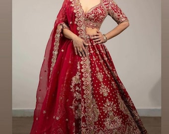 May include: A vibrant red lehenga with intricate gold embroidery. The ensemble includes a matching dupatta and a cropped top with a plunging neckline. The skirt features detailed floral patterns, creating an elegant and festive look.