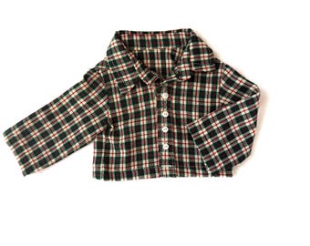 May include: A green, red, and black plaid button-down shirt with long sleeves. The shirt has a collar and white buttons down the front. The fabric appears to be a soft flannel or similar material, suitable for cooler weather.