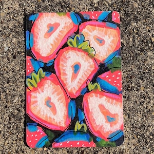May include: A colorful, rectangular artwork featuring a pattern of sliced strawberries. The strawberries are painted in shades of red, pink, and orange, with green leaves and blue accents against a black background. The artwork is on a textured surface.