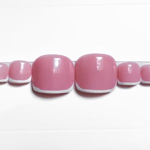May include: A set of ten artificial toenails in a light pink color with a white French tip design. The nails are arranged in a row on a clear adhesive strip, ready for application. The nails are glossy and have a rounded shape.
