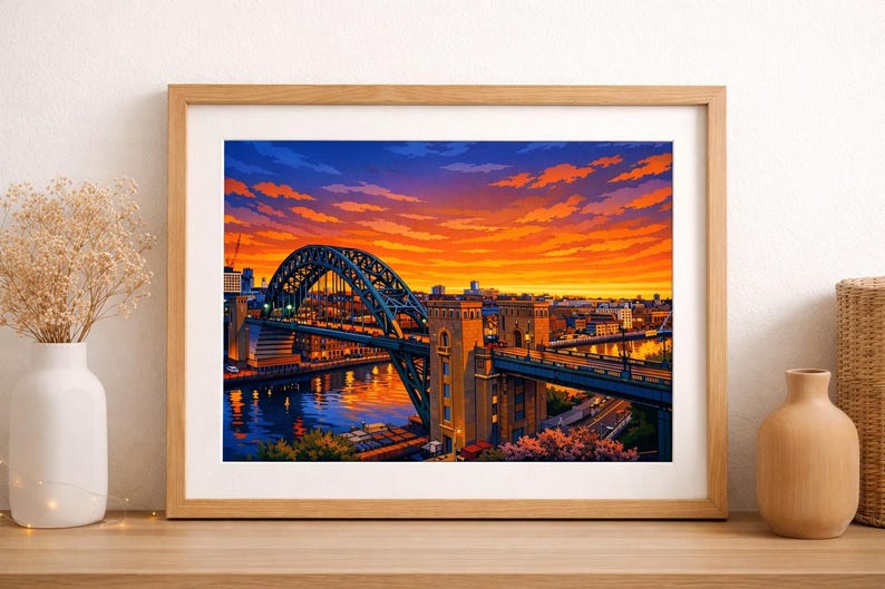 May include: A framed print of a bridge over a river at sunset. The bridge, with its distinctive arch, is rendered in blue and green hues. The sky is a striking blend of orange, yellow, and blue. The artwork is presented on a wooden surface.