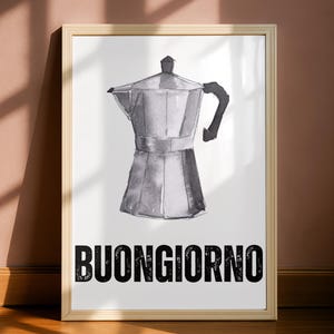 May include: A framed print featuring a watercolor illustration of a stovetop espresso maker in shades of gray. The word "BUONGIORNO" is printed in bold black letters at the bottom of the image. The frame is a light wood color.