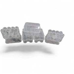 May include: Several clear plastic egg cartons with lids are stacked and arranged on a white background. The cartons are designed to hold a dozen eggs each. The image shows the cartons from a slightly elevated angle.