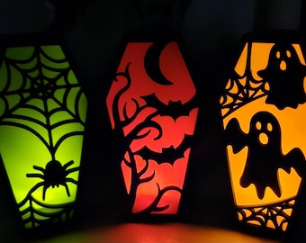 May include: Three coffin-shaped Halloween decorations with illuminated interiors. One glows green with a spiderweb and spider, another red with bats and branches, and the last orange with ghosts and a web.