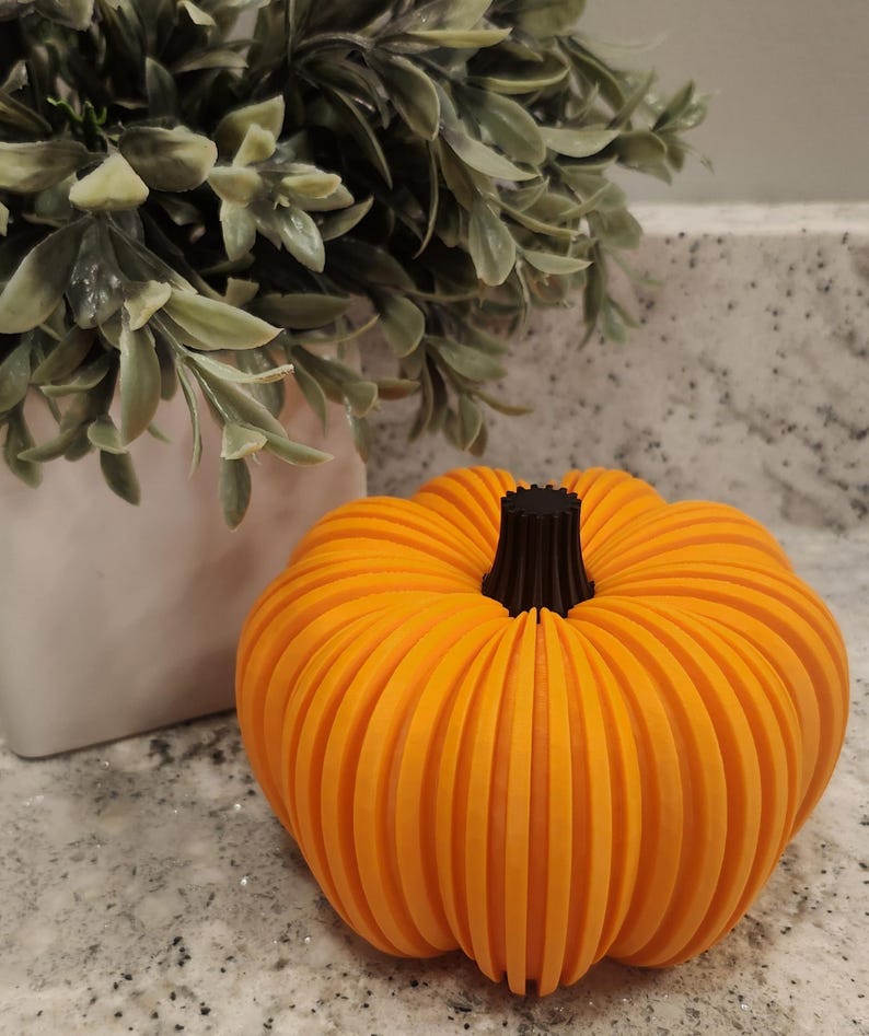May include: An orange, ribbed pumpkin with a black stem. The decorative pumpkin is a fall-themed item, perfect for seasonal home decor. The pumpkin is approximately 6 inches in diameter.